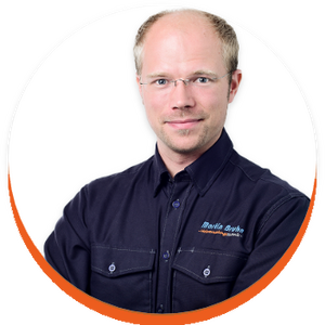 Porträt von Martin Bruhn in einer Kreisgrafik mit weißen Hintergrund. Er trägt ein dunkelblaues Hemd und Brille.